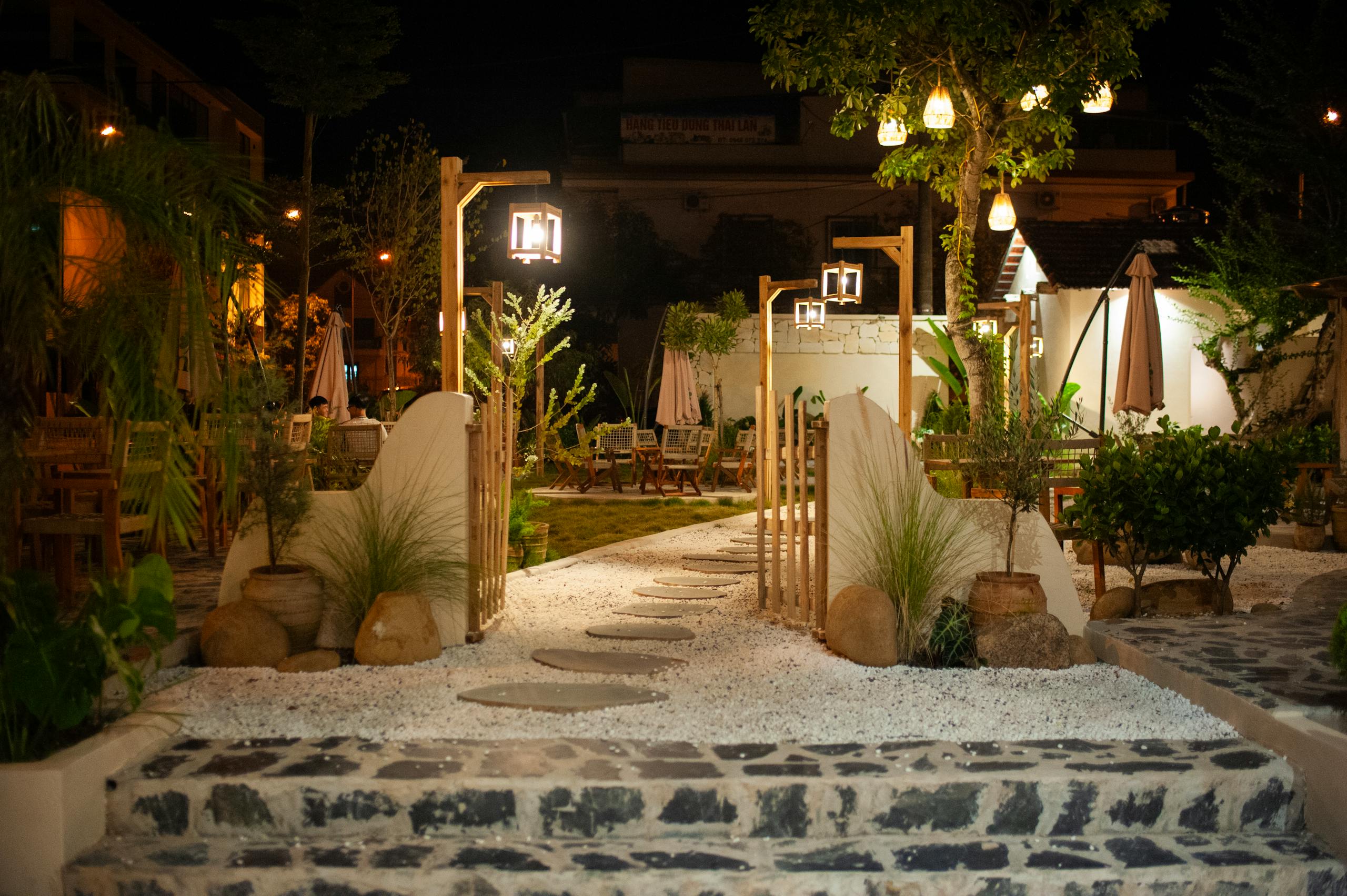 Beautifully lit outdoor garden dining area at night, with lush greenery and elegant lighting.